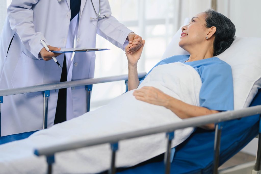 A nurse holding the hand of an older patient in a hospital bed